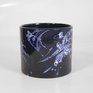 May include: A black ceramic planter with a white and blue marbled design. The planter is cylindrical in shape and has a smooth, glossy finish.