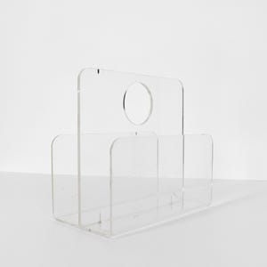 May include: A clear acrylic magazine rack with a handle. The rack has two compartments and a circular cutout in the top.