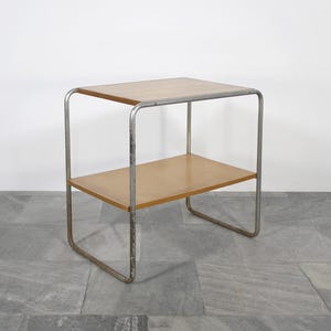 May include: A small, two-tiered side table with a light wood top and shelf. The frame is made of silver-colored metal. The table is approximately 24 inches tall, 20 inches wide, and 14 inches deep.
