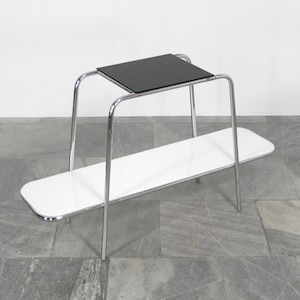 May include: A chrome two-tiered table with a black top shelf and a white bottom shelf. The table has a modern design with rounded edges.