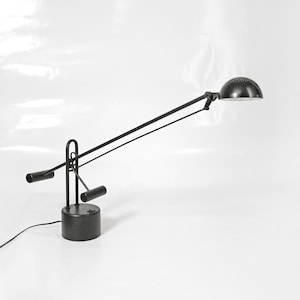 May include: A black desk lamp with a long, articulated arm and a round, white shade. The lamp has a black base and a cord.