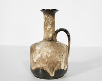 May include: A ceramic vase with a dark brown base and rim, a light brown body with white dripped glaze, and a curved handle. The vase has a narrow neck and a rounded body. The overall design is vintage and decorative.