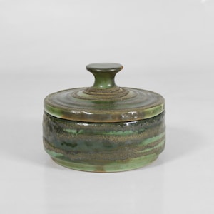 May include: A green ceramic jar with a lid and a knob on top. The jar has a mottled green glaze with brown accents.