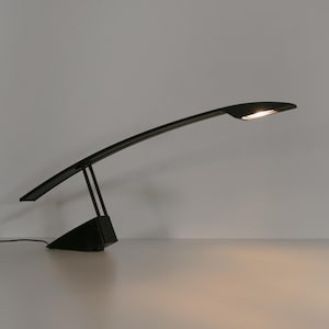 May include: A black desk lamp with a long, curved arm and a rectangular base. The lamp is switched on and the light is shining.