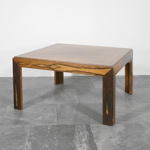 May include: A square wooden coffee table with a dark wood grain pattern. The table has a simple design with four legs and a flat top.