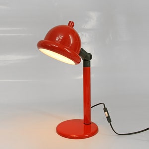 May include: A red desk lamp with a round, dome-shaped shade and a black switch on the cord.