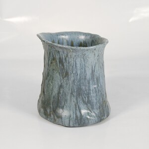 May include: A blue ceramic vase with a textured surface that resembles tree bark. The vase has a wide mouth and a rounded base.