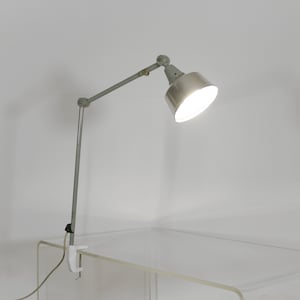 May include: A silver adjustable desk lamp with a clamp base. The lamp is on and illuminating the room.