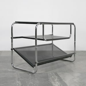 Puede incluir: Una estantería de tres niveles de metal cromado y negro con un estante inferior inclinado.