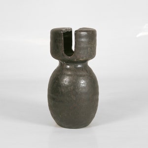 May include: A dark brown ceramic vase with a unique shape. The vase has a rounded base and a cylindrical neck with a U-shaped opening at the top. The surface has a textured appearance.