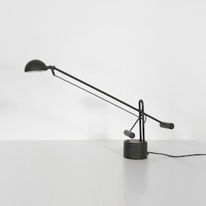 May include: A black desk lamp with a long, articulated arm and a round, black shade. The lamp has a black base and a black cord.