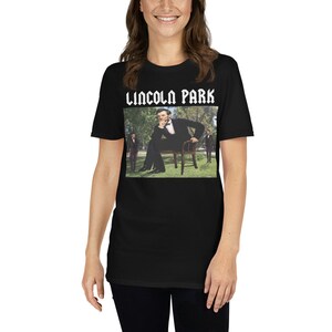 May include: Black t-shirt with a white graphic of a man sitting on a chair in a park. The text "LINCOLN PARK" is above the image.