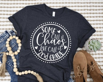 May include: A dark blue t-shirt with a white circle design that says "Some call it chaos we call it 2nd grade" with hearts around the text.