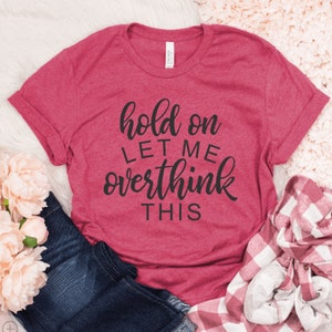 May include: A pink t-shirt with the text "hold on let me overthink this" in black script.