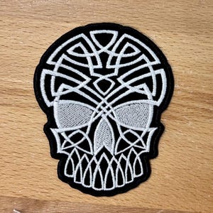 May include: White embroidered skull patch with a Celtic knot design on a black background.
