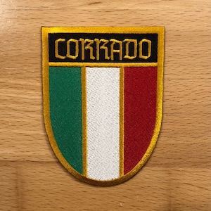 May include: A gold embroidered patch with the word "Corrado" in black lettering and the Italian flag colors of green, white, and red.