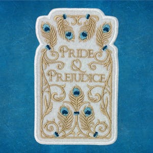 Pode incluir: Patch de feltro branco com bordado dourado que representa uma capa de livro com o título "Pride & Prejudice" e penas de pavão.
