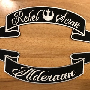 Op de afbeelding: Twee zwarte geborduurde patches met witte stiksels. De bovenste patch heeft de tekst "Rebel Scum" met het Rebel Alliance-symbool in het midden. De onderste patch heeft de tekst "Alderaan".