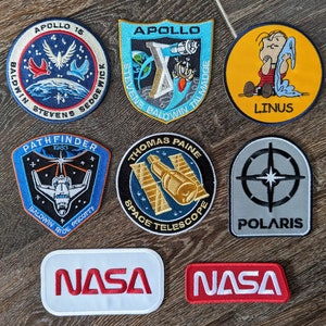 Peut inclure: Neuf patchs brodés avec différents logos de missions de la NASA, dont Apollo 15, Pathfinder, télescope spatial Thomas Paine et Polaris. Deux patchs affichent "NASA" en lettres rouges.