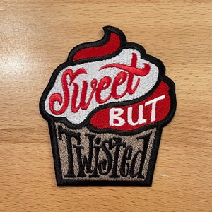 Puede incluir: Un parche bordado con forma de cupcake con el texto "Sweet But Twisted" en rojo, blanco y negro.
