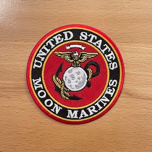 Può includere: Una toppa ricamata in rosso, bianco e oro con le parole "United States Marine Corps" in un cerchio. La toppa presenta un globo con un'ancora e un'aquila.