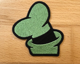 May include: Green embroidered patch of a cartoon character's hat. The hat is green with a black brim and a green top.
