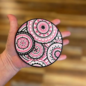 Pode incluir: Um remendo redondo branco com um design de mandala rosa e preto. O mandala apresenta padrões circulares intrincados e motivos florais.