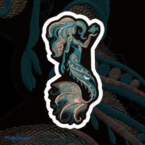 May include: An embroidered mermaid in teal and gold with a white outline. The mermaid is in a stylised design with a flowing tail and hair.