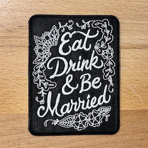 May include: Black embroidered patch with white lettering that reads "Eat Drink & Be Married" surrounded by a floral design.