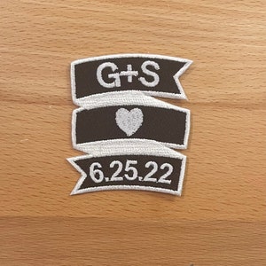 Könnte beinhalten: Drei braune Stoffbanner mit weißen Nähten. Das obere Banner sagt "G+S". Das mittlere Banner hat ein weißes Herz. Das untere Banner sagt "6.25.22".