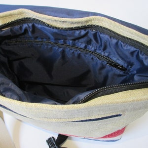 May include: A beige canvas messenger bag with a blue lining and a black zipper. The bag has a red, white and blue stripe pattern on the bottom.