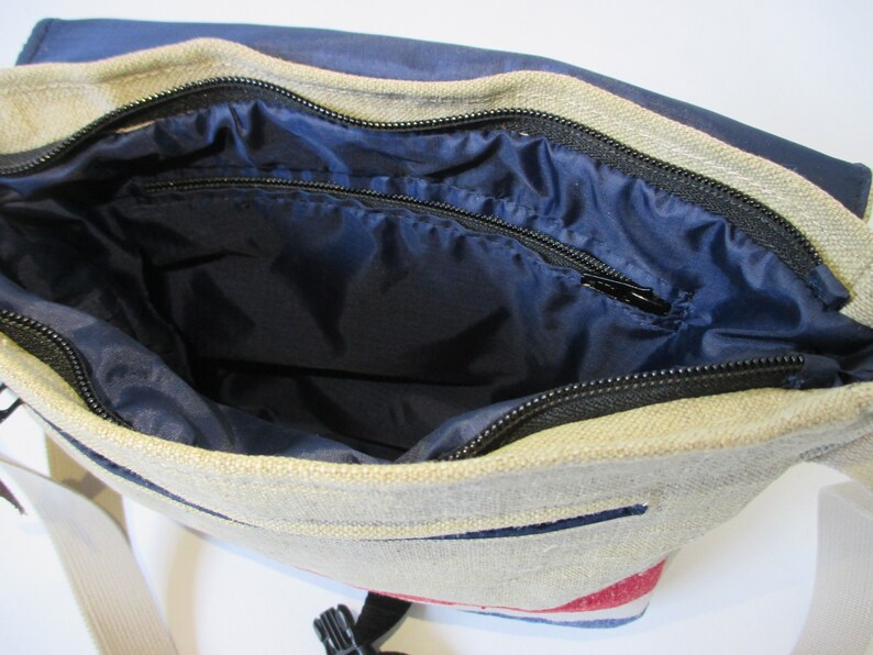 May include: A beige canvas messenger bag with a blue lining and a black zipper. The bag has a red, white and blue stripe pattern on the bottom.