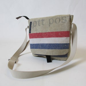 May include: A beige canvas messenger bag with a red, white and blue striped design. The bag has a black adjustable strap and the text "ptt pos" is printed on the front.