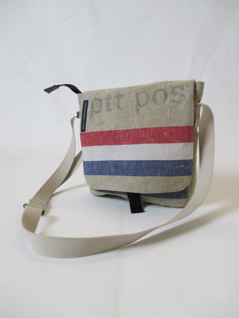 May include: A beige canvas messenger bag with a red, white and blue striped design. The bag has a black adjustable strap and the text "ptt pos" is printed on the front.