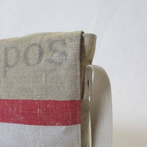 May include: A beige canvas messenger bag with a red, white and blue striped pattern. The bag has a long, adjustable strap and the word "POS" is printed on the front.