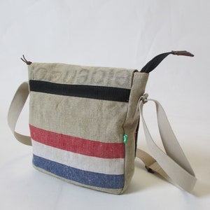 May include: A beige canvas messenger bag with a black strap and red, white and blue stripes. The bag has a brown leather handle and a green label.