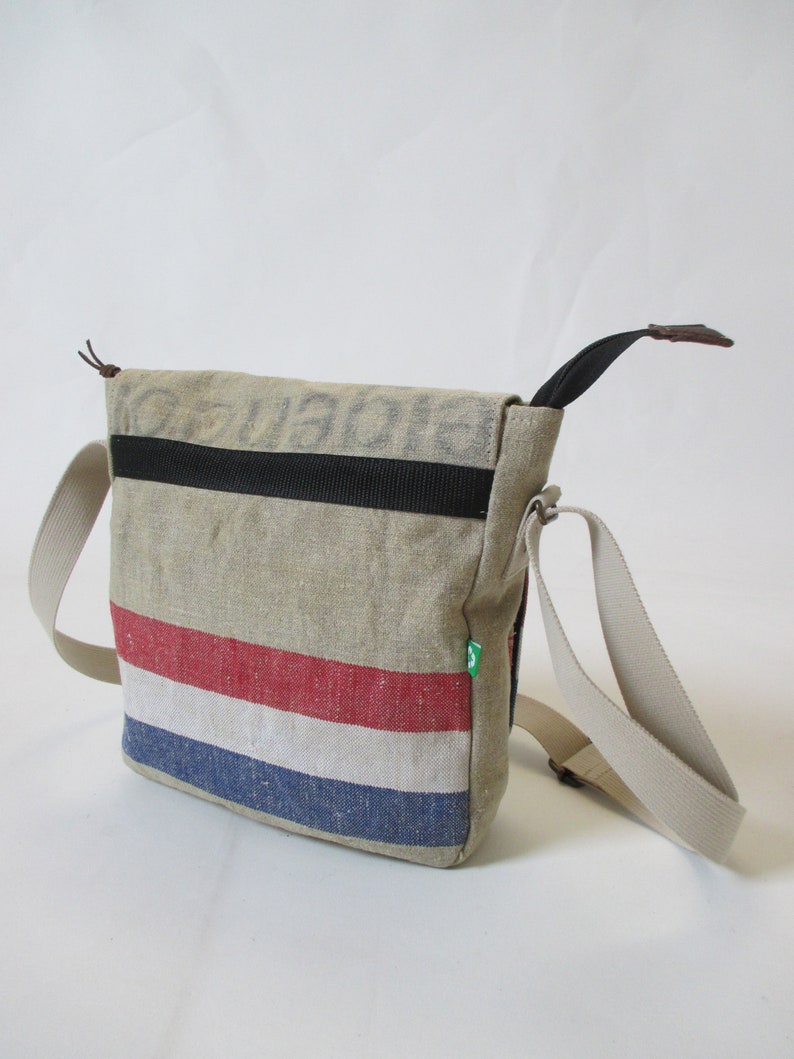 May include: A beige canvas messenger bag with a black strap and red, white and blue stripes. The bag has a brown leather handle and a green label.