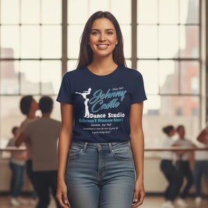 May include: A navy blue t-shirt with the text "Johnny Castle Dance Studio" in white and light blue. The shirt features a dancer graphic and additional text below. The person is wearing blue jeans.