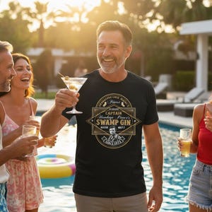 May include: A black t-shirt with a gold and white graphic that reads "Captain Hamlage Pierce's Swamp Gin" with a portrait and the text "Since 1973". The man is holding a martini glass with olives.
