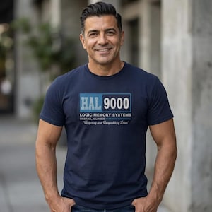 Puede incluir: Camiseta azul marino con el texto "HAL 9000" en un diseño rectangular. Debajo, se lee "Logic Memory Systems, Urbana, Illinois" y la frase "Foolproof and Incapable of Error".