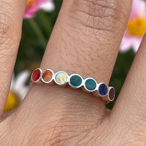 May include: A silver ring with a rainbow of colorful stones set in a circle. The stones are red, orange, yellow, green, blue, indigo, and violet.