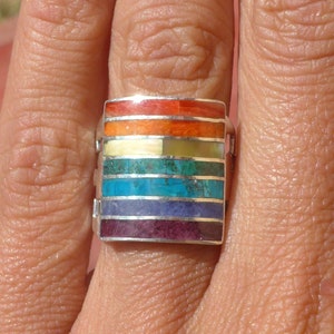 May include: A silver ring with a rectangular inlay of colourful stones. The stones are arranged in a rainbow pattern, with red, orange, yellow, green, blue, indigo, and violet.