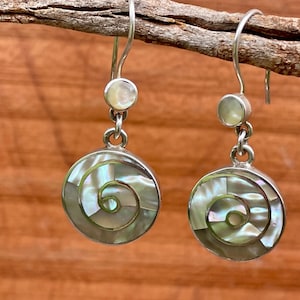 May include: Silver earrings with a spiral design. Each earring has a round, iridescent mother-of-pearl inlay with a spiral pattern. A smaller, round pearl sits above the main design.