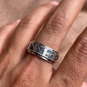 May include: A silver spinning ring with a decorative design. The ring is worn on a person's finger.