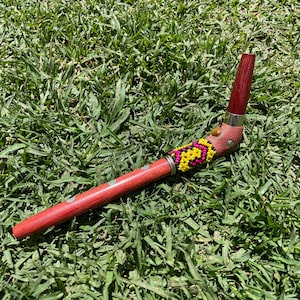 May include: A red wooden pipe with a beaded design in pink, yellow, and black. The pipe is bent at a 90-degree angle and has a silver metal band.