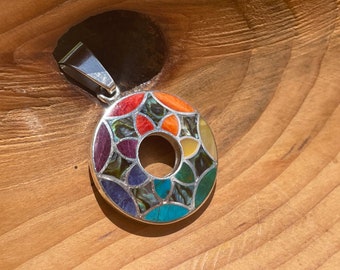 May include: A round silver pendant with a colorful mosaic design. The mosaic is made of various stones, including turquoise, abalone, and coral. The pendant has a hole in the center for a chain.