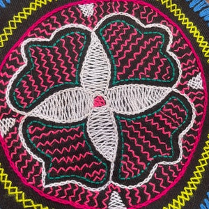 Könnte beinhalten: Ein rundes Stickmuster mit schwarzem Hintergrund und einem weißen, grünen und rosa Blumenmuster. Das Muster ist von einem gelben und blauen Rand umgeben.
