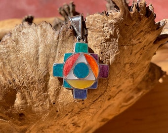 May include: A silver pendant with a colorful Aztec cross design. The cross is made of turquoise, red, orange, yellow, and purple stones.