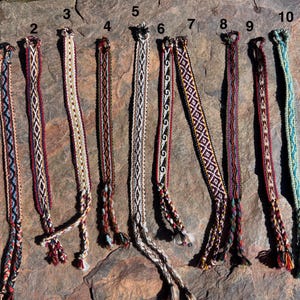 May include: Ten woven fabric bracelets numbered one through ten, featuring various geometric patterns and color combinations including red, blue, white, brown, black, and teal. Each bracelet has a loop at one end and braided ties at the other.