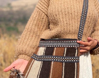 May include: A brown and white striped woven bag with a black and white geometric pattern. The bag has two brown tassels and a long strap with a black and white geometric pattern.